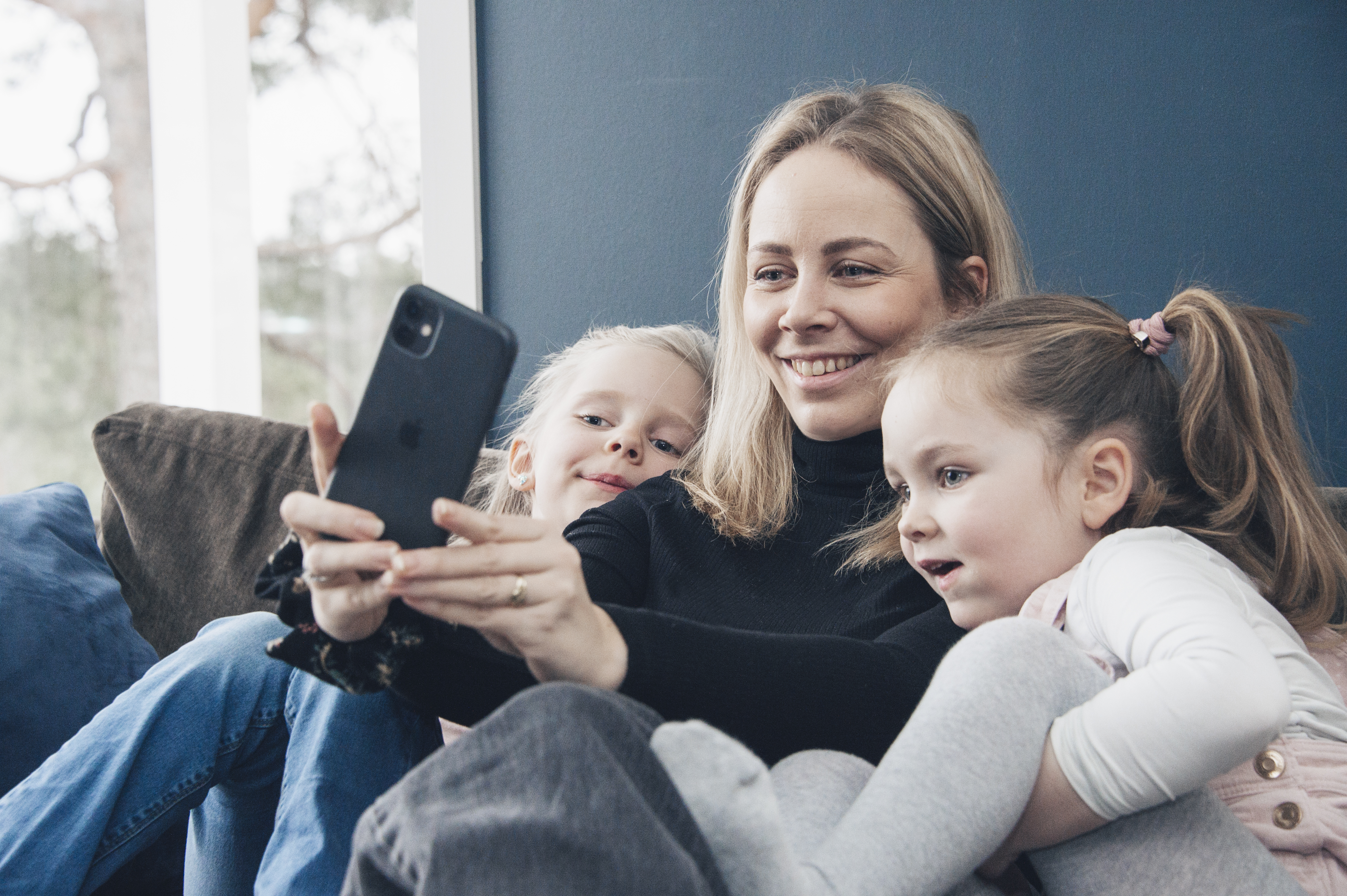 En mor sitter sammen med sine to småbarn og ser på en mobiltelefon