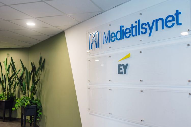 Bilete frå inngangspartiet til Medietilsynets kontor. Medietilsynets logo i blått mot kvit bakgrunn på veggen. Ein grøn plante i hjørnet.