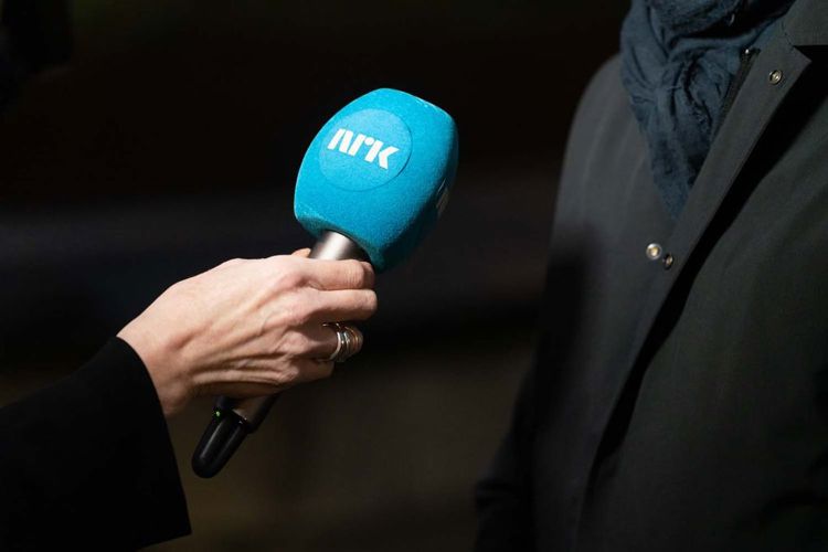 En NRK-mikrofon mellom intervjuer og intervjuobjekt. Nærbilde av hånd og mikrofon, vi ser ikke personene.