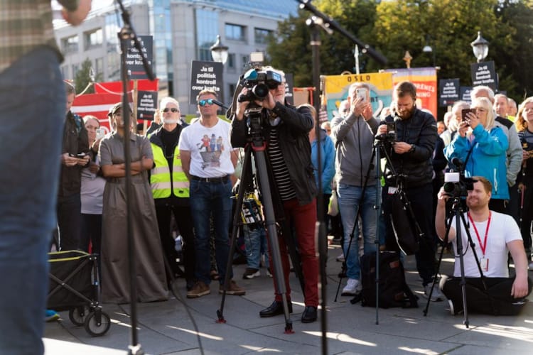 Foto- og videojournalister i arbeid under en demonstrasjon ved Stortinget. Bak dem er det demonstranter og paroler.