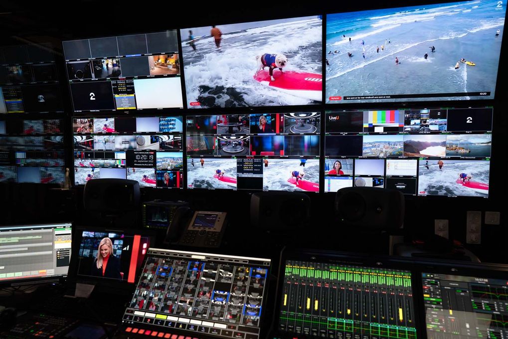 Regi-panel og tv-skjermer. Knapper og spaker i forgrunnen og store skjermer med mange forskjellige bilder på veggen bak.