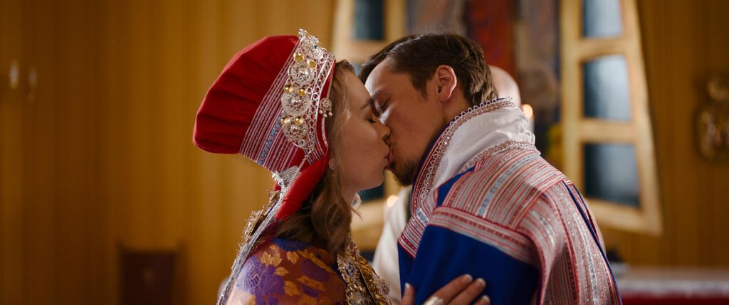 Brudepar i tradisjonelle samiske festdrakter kysser hverandre innendørs under en bryllupsseremoni.