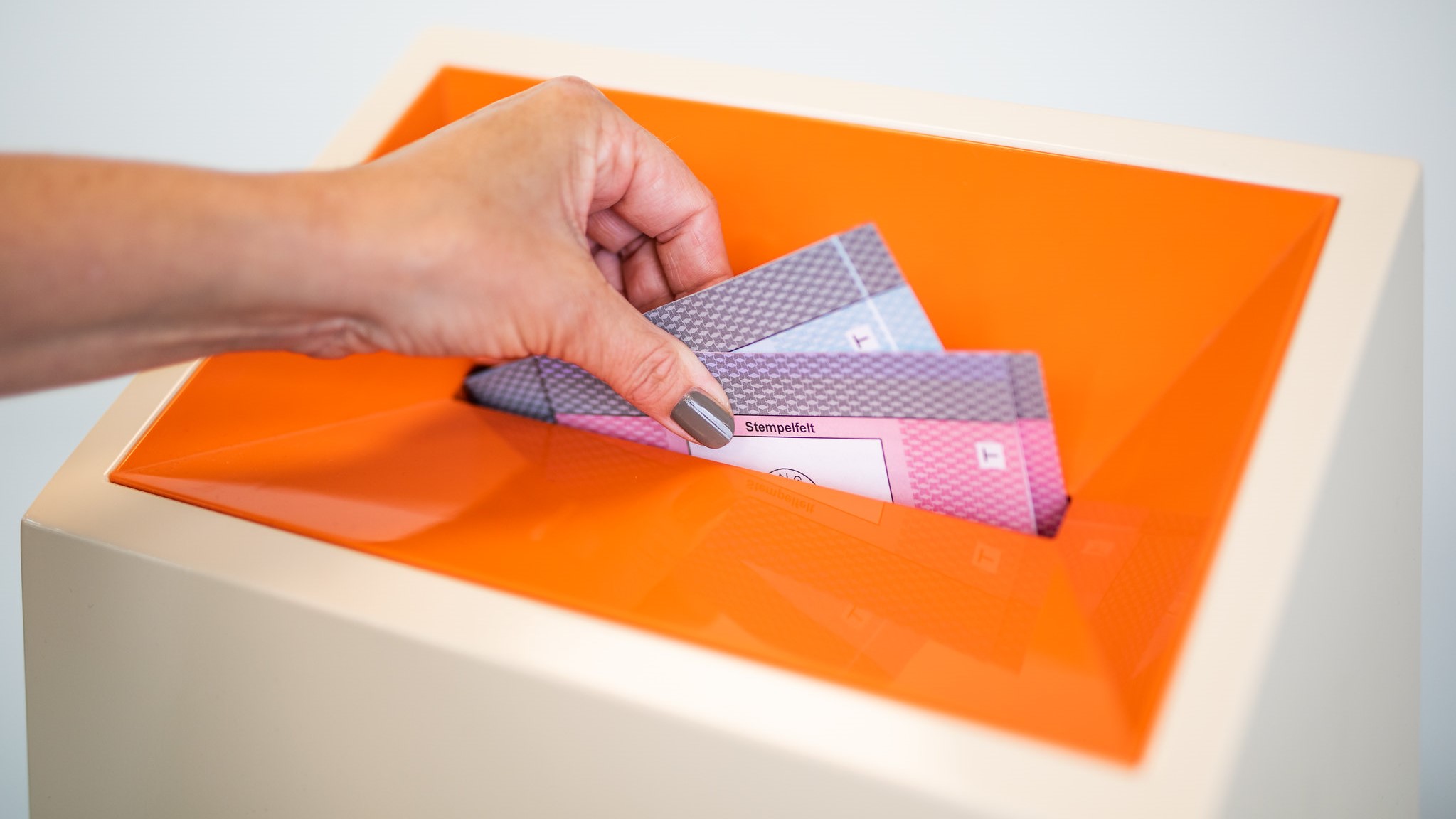 H&aring;nd som legger stemmesedler i en oransje valgurne, sett i n&aelig;rbilde.