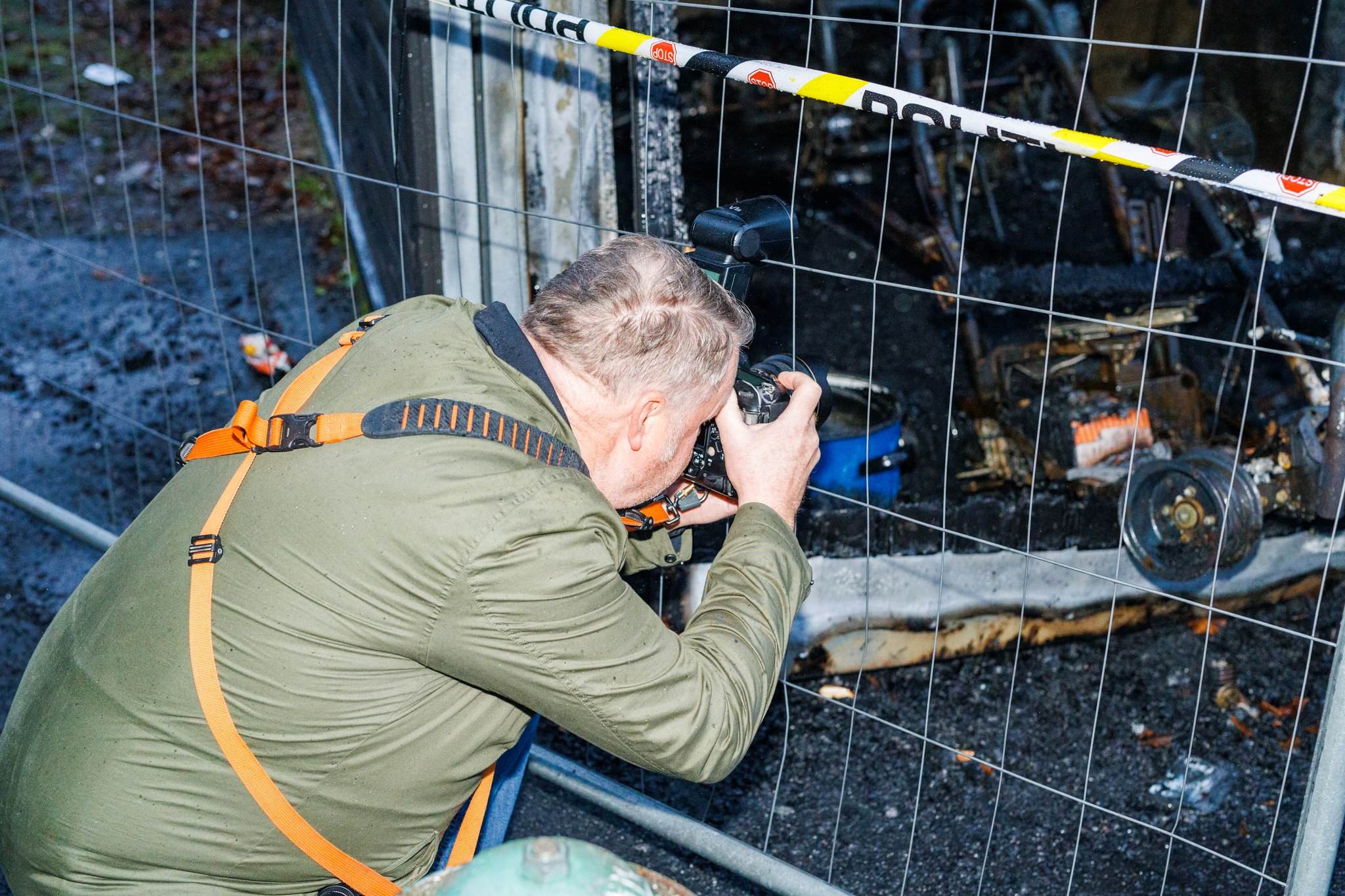 Fotograf dokumenterer brannskadet omr&aring;de bak gjerde med kamera.
