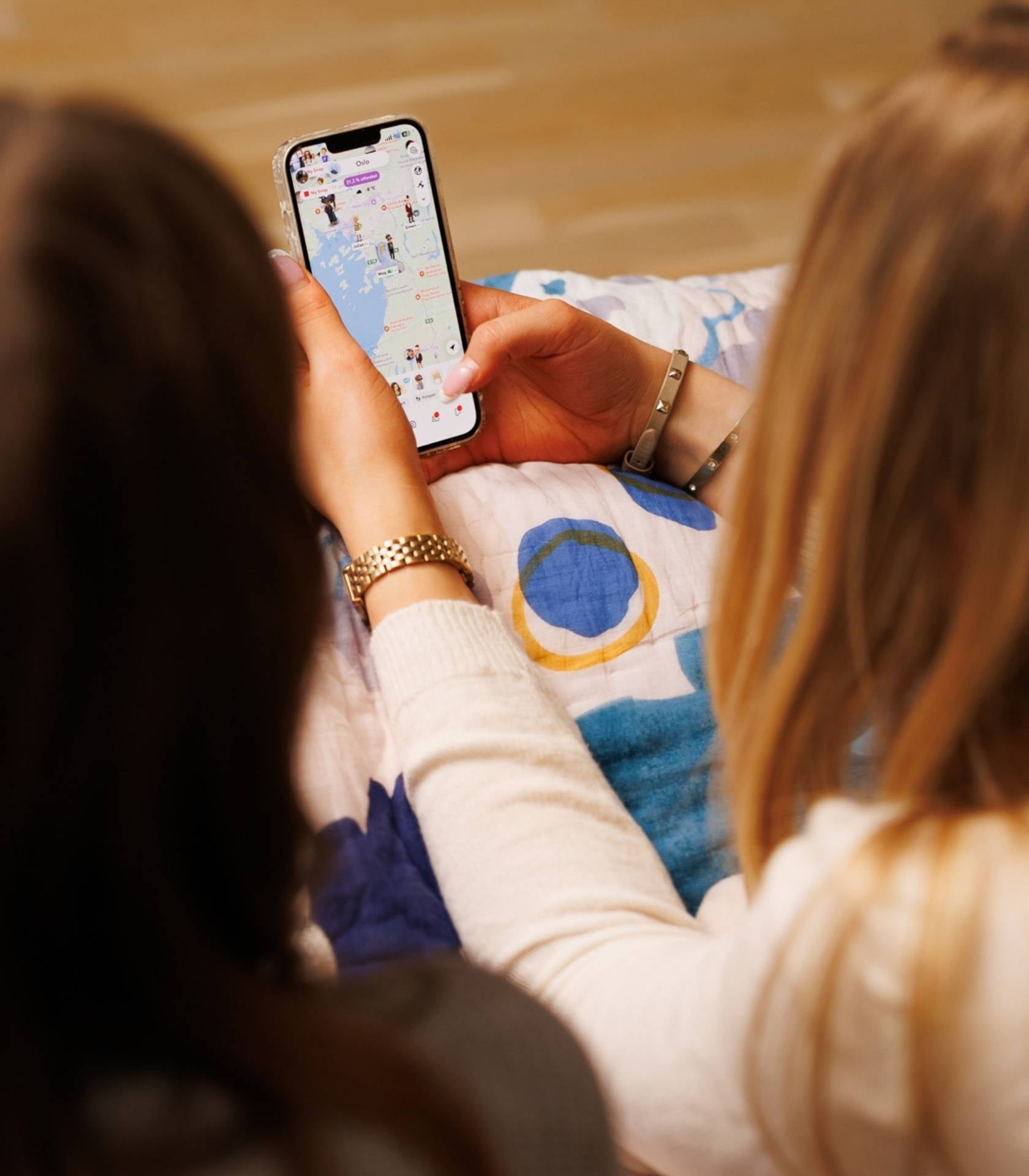 To unge sitter sammen og ser på en mobiltelefon som viser et digitalt kart med profiler og markører.